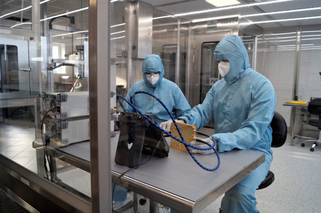 Two SpaceForest engineers dressed in protective suits, working in the cleanroom on the SSPA device.