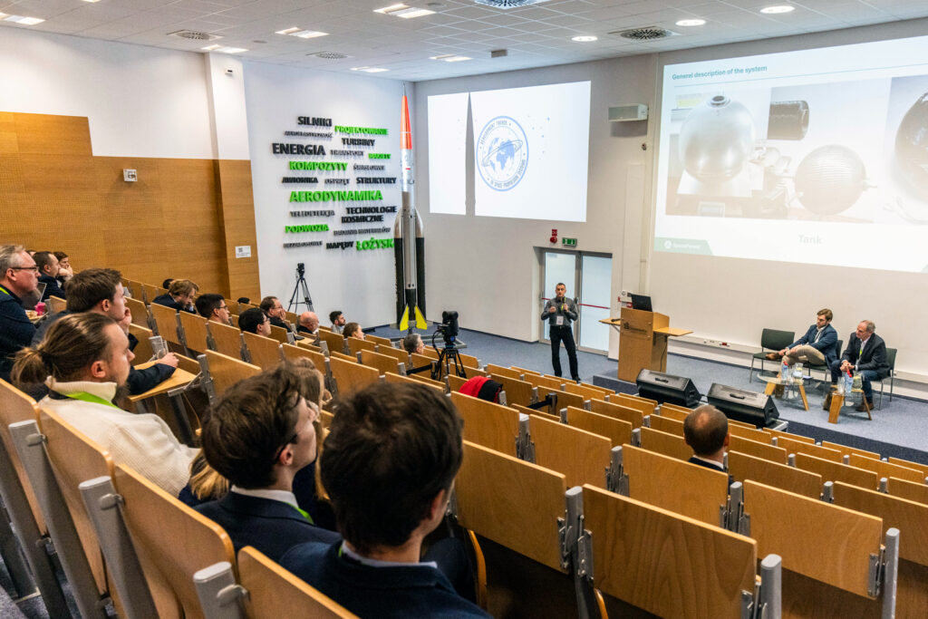 PhD Adam Matusiewicz presenting the SALTO project at SpaceTrends 2024 conference, with the audience prominently visible in the background.