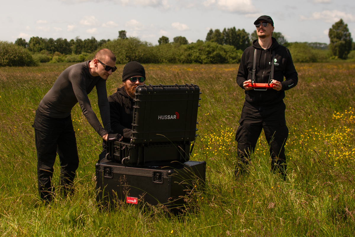HUSSAR SAR radar system operators in the field, preparing equipment for operation. Transport case with HUSSAR logo visible.