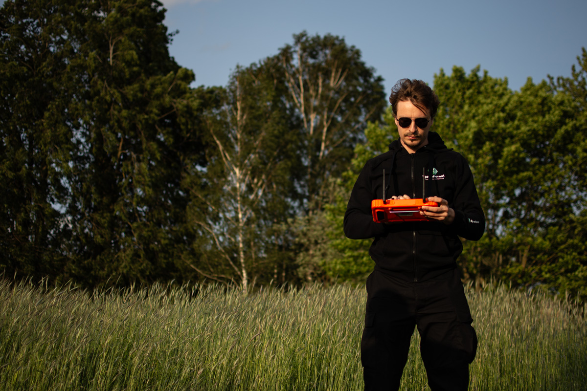 Drone operator with a handheld controller overseeing the HUSSAR SAR system in open-field operation.