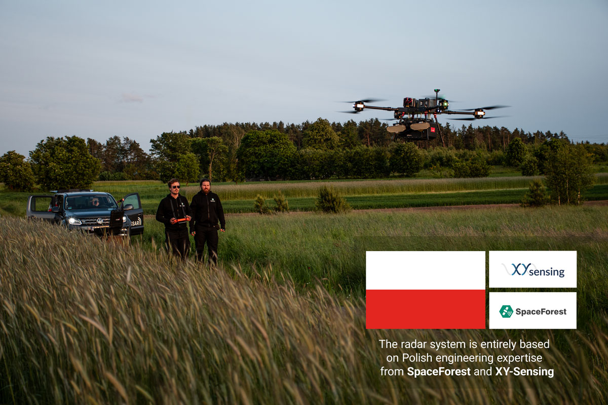 A drone with the HUSSAR SAR radar system in flight over a field, featuring the logos of SpaceForest and XY-Sensing, and the Polish flag.